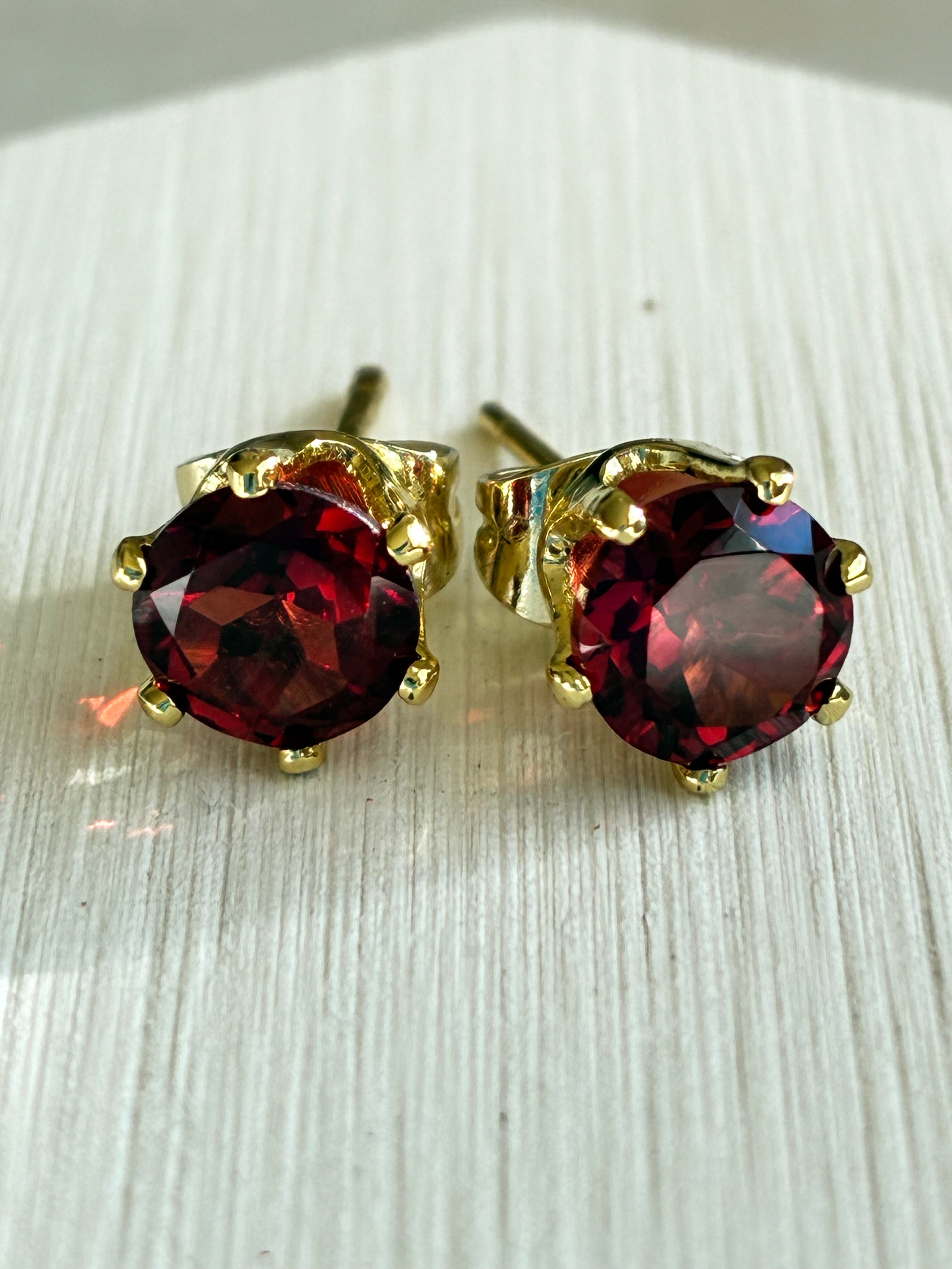 Pair of garnet gemstone stud earrings with gold settings on a light wooden surface.