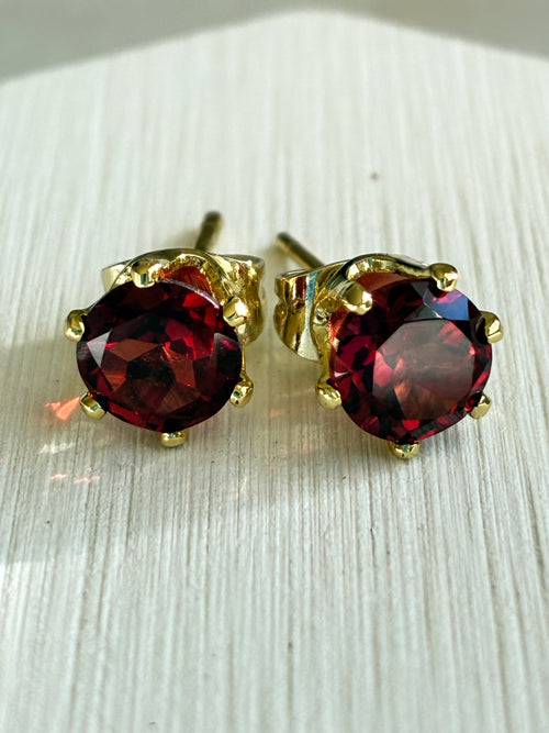 Pair of garnet gemstone stud earrings with gold settings on a light wooden surface.