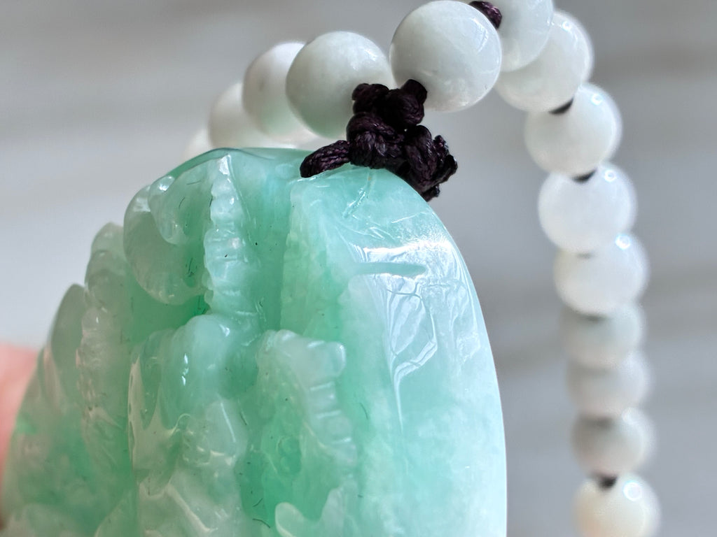 Green jade pendant with white beads on a blurred background