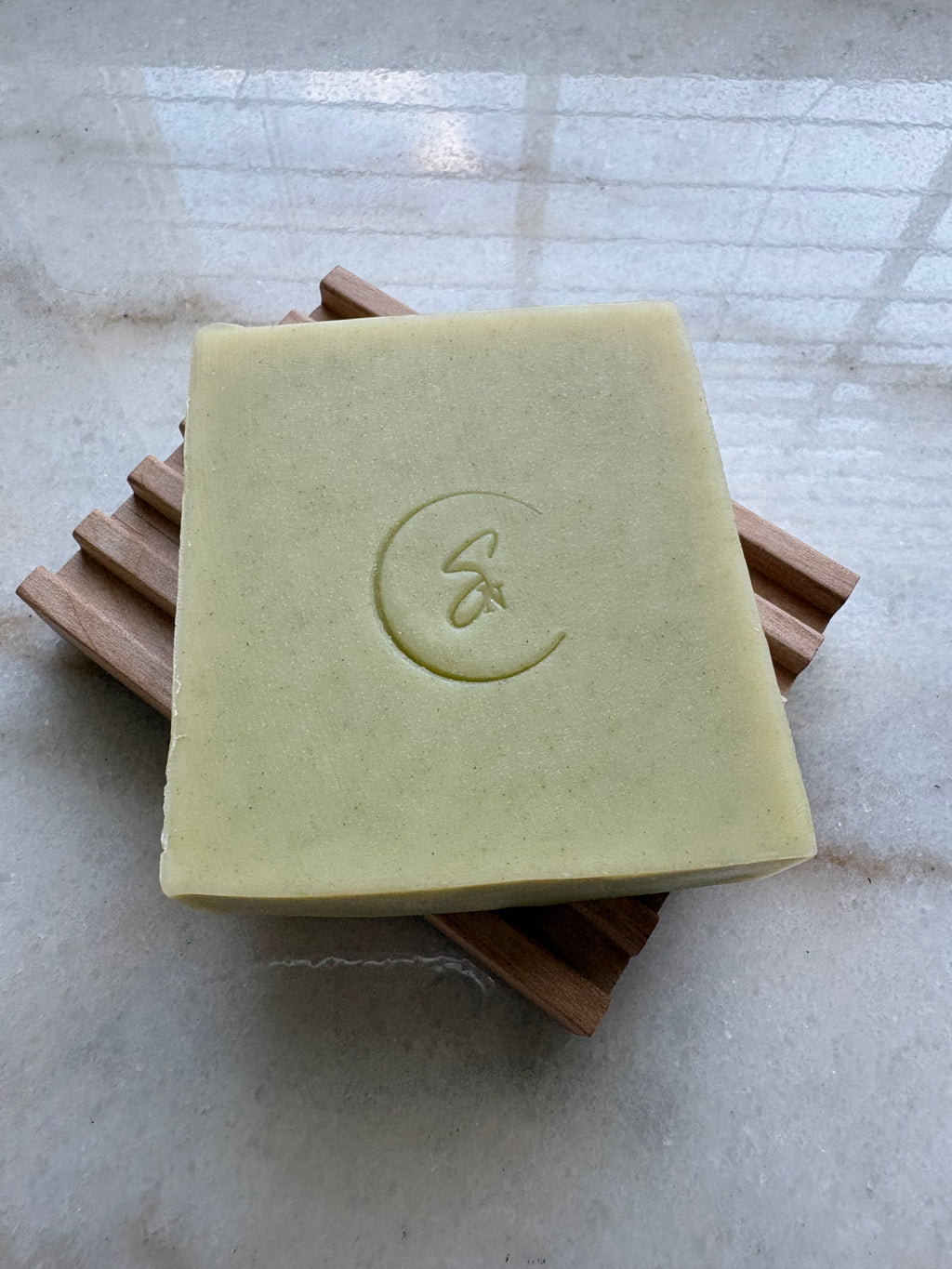 Handmade cucumber and aloe vera soap displayed on a natural wooden soap dish.