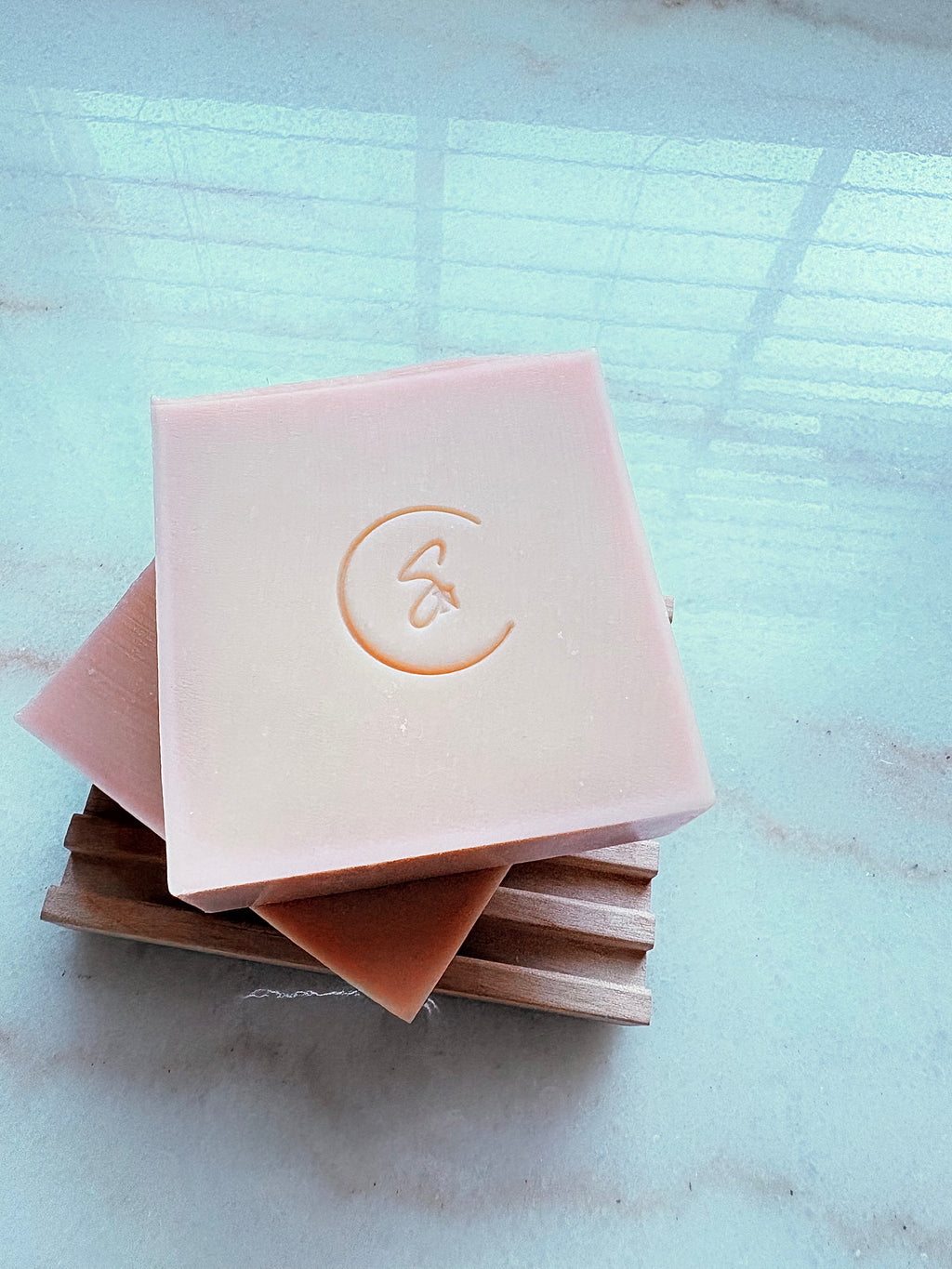 Rose soaps stacked on a wooden soap dish over a marble surface.