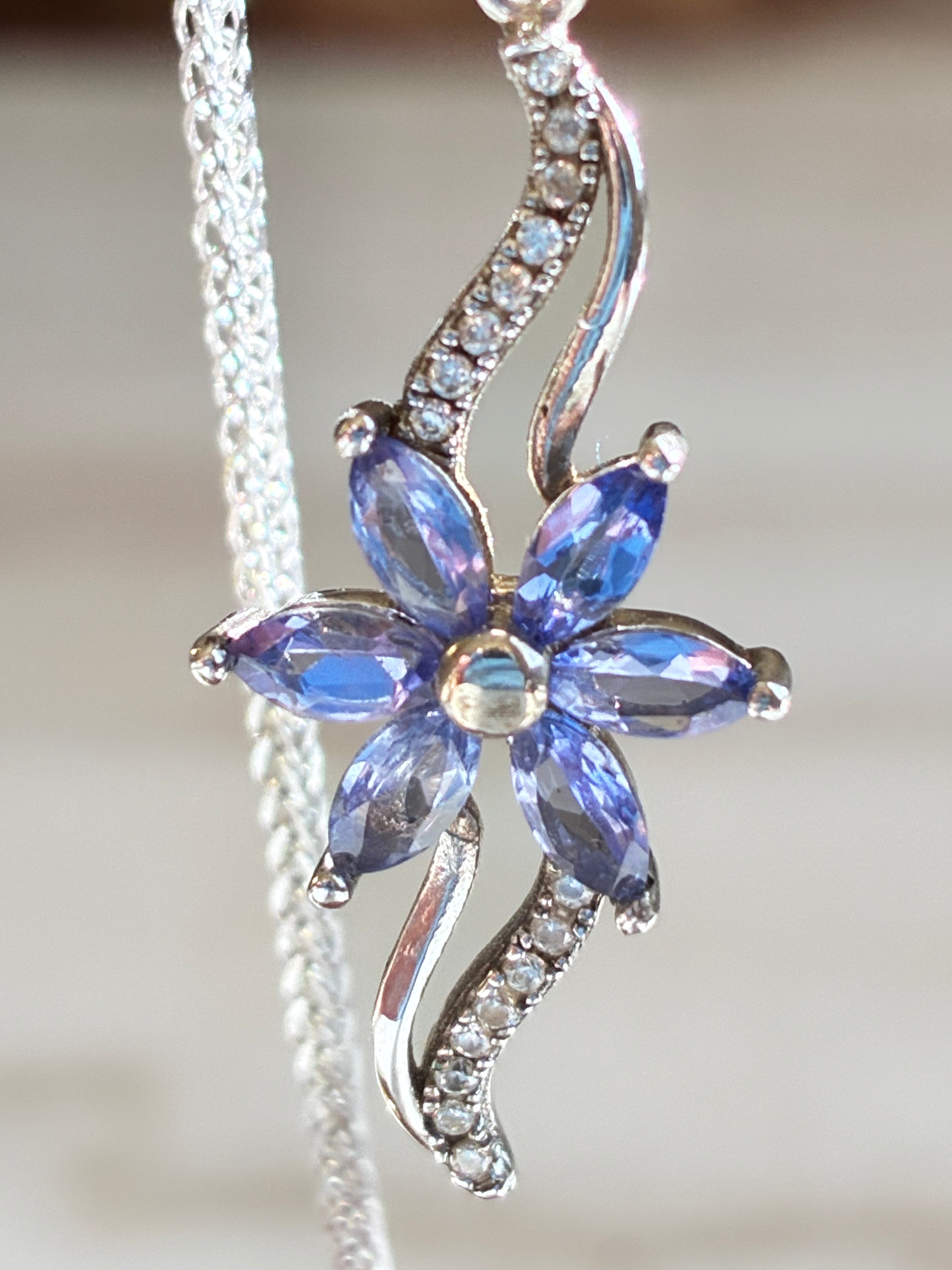 Blue flower-shaped pendant with gemstones on a silver chain against a blurred background