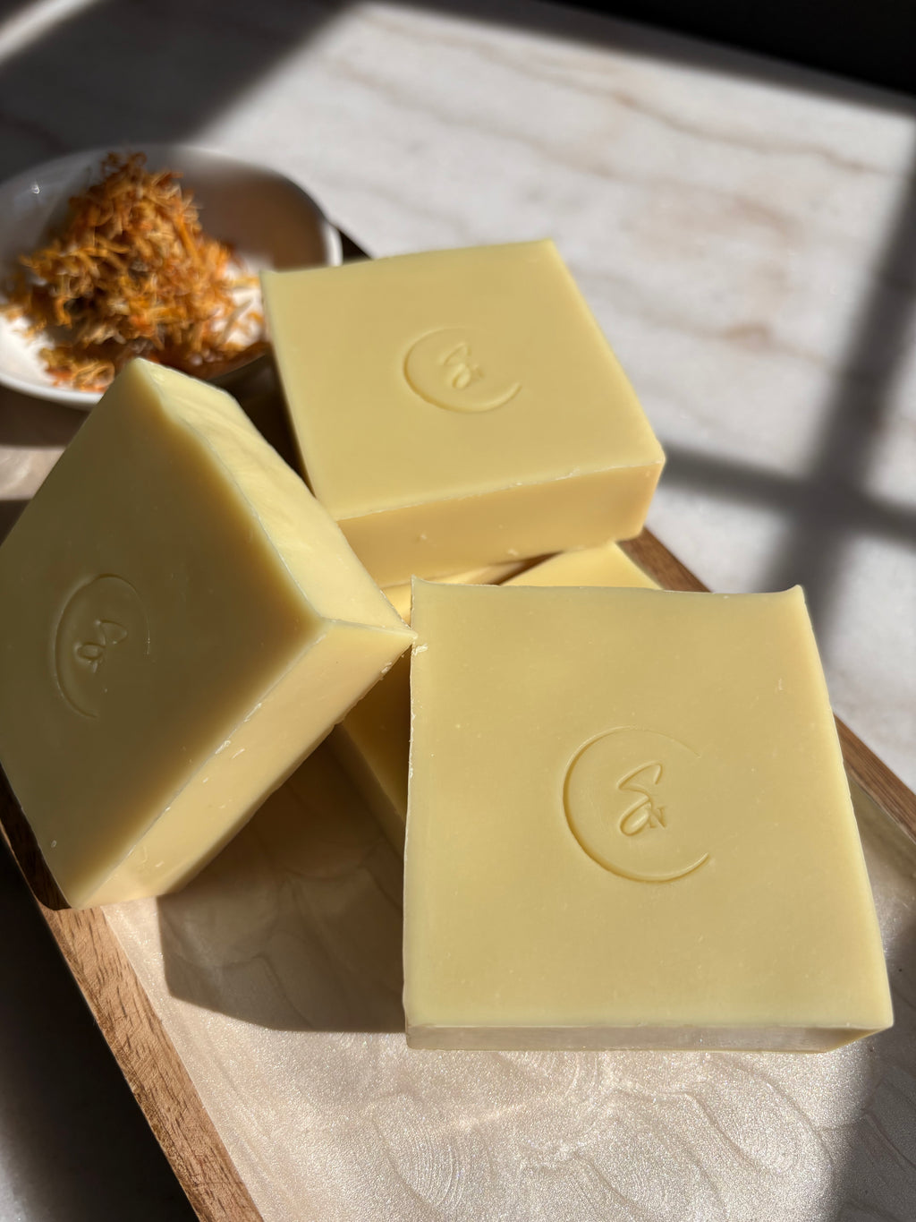 A golden-yellow Calendula Crest soap bar with visible dried orange calendula petals embedded throughout for natural exfoliation.