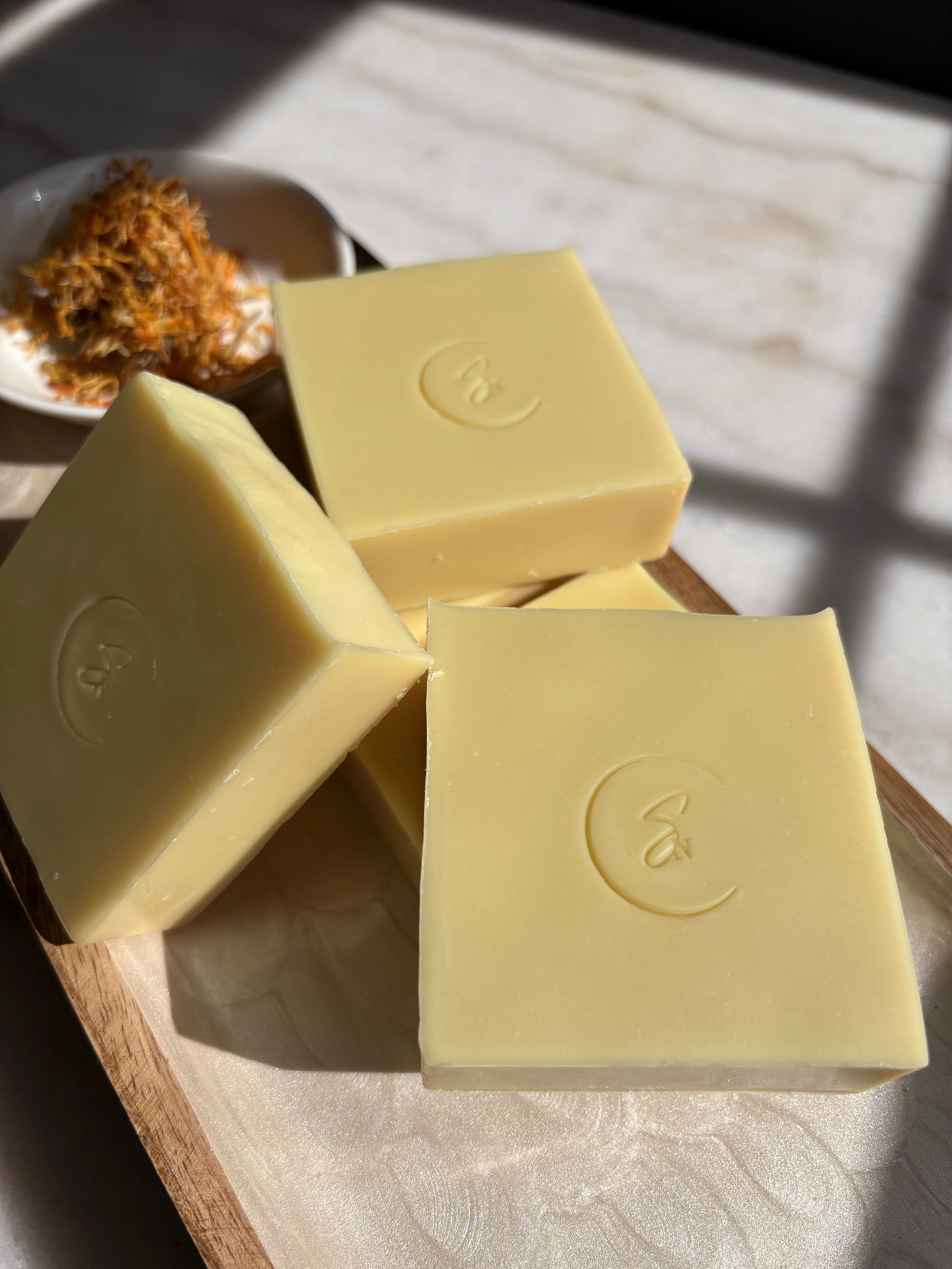 A golden-yellow Calendula Crest soap bar with visible dried orange calendula petals embedded throughout for natural exfoliation.
