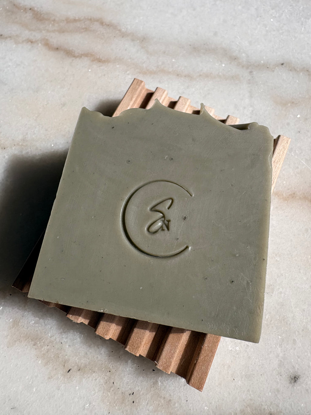 The Alpine Moss beauty bar resting on a wooden soap dish